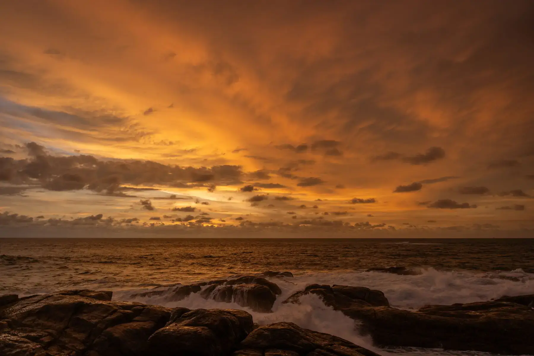A vibrant orange sunset over a rocky Sri Lankan coastline.