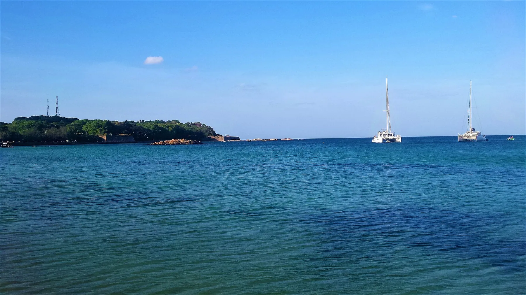 A calm blue bay at Trincomalee with two catamarans at anchor and a wooded headland on the left.