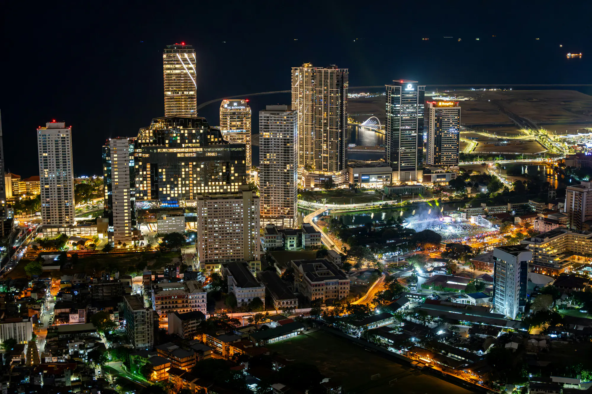 Colombo's skyline at night seen from above, the golden-lit Lotus Tower rising among the illuminated high-rises along the waterfront.
