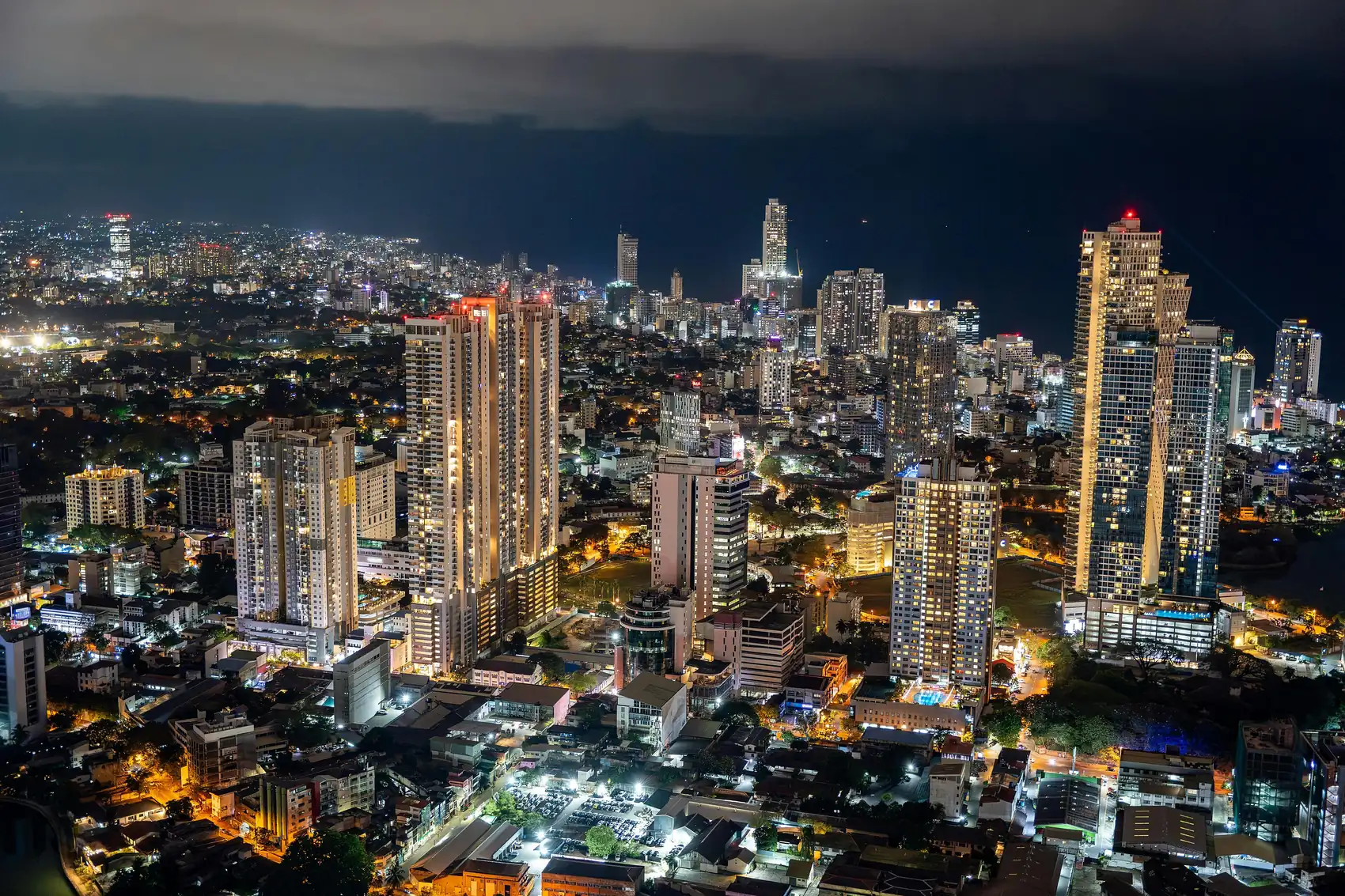 The Colombo city skyline at night, with lit towers and their reflections under a dark sky.