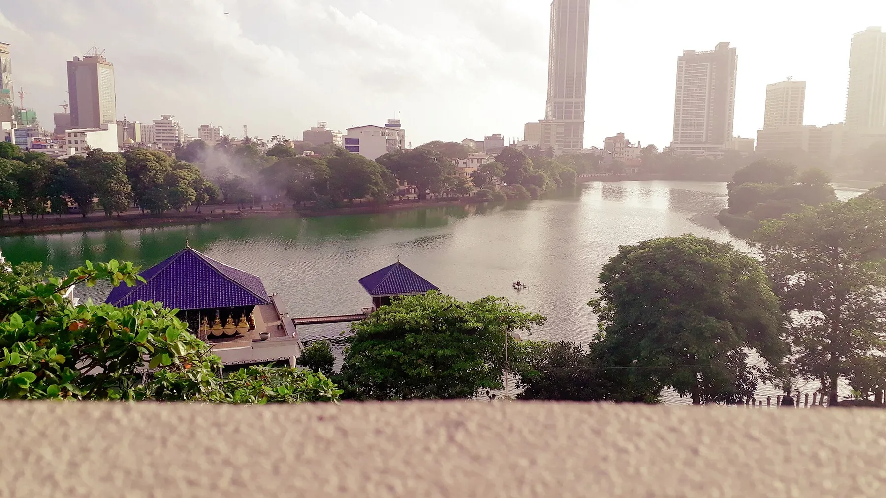 The blue roofs of the Seema Malaka temple of Gangaramaya on Beira Lake in Colombo, with city towers behind.