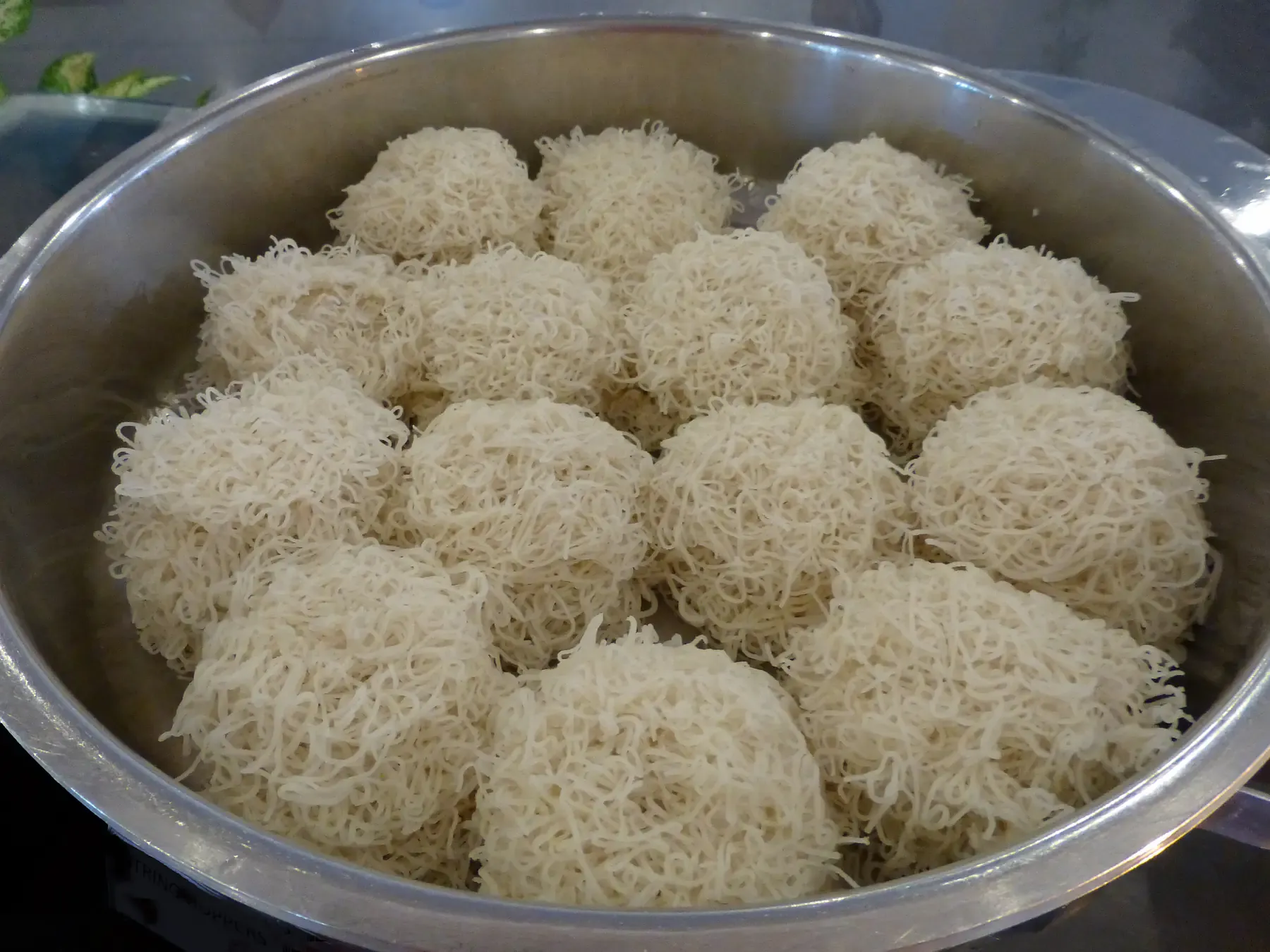 Steamed string hoppers, round nests of rice-flour noodles, in a metal steamer tray.