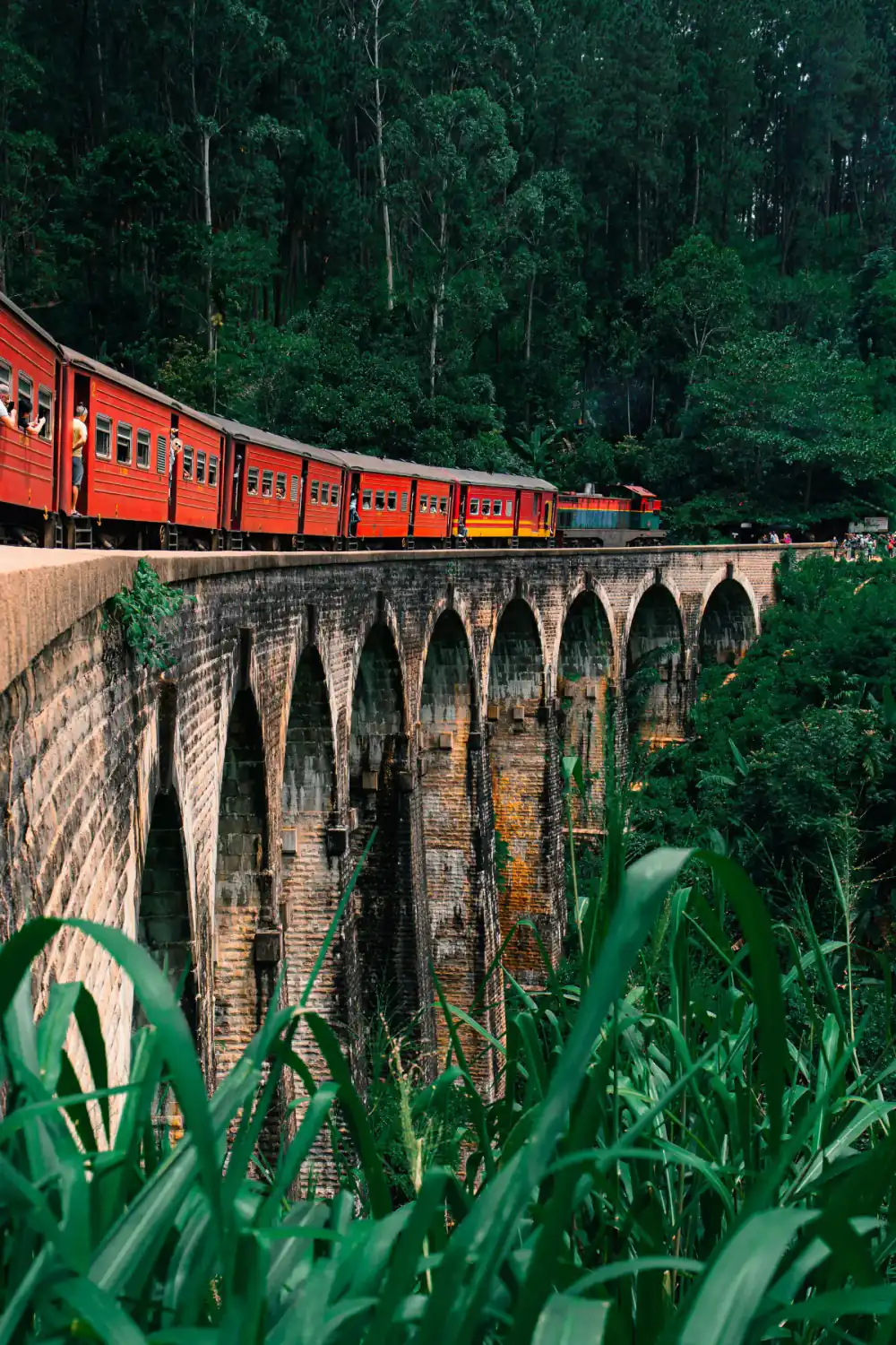 A red train crossing the historic Nine Arch Bridge.
