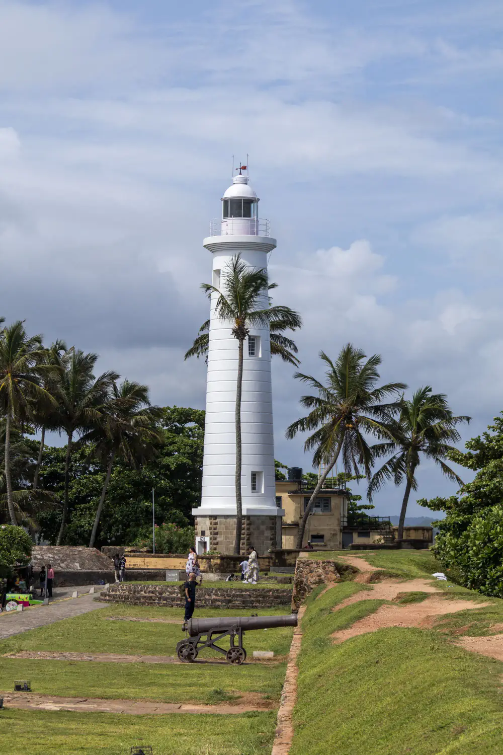 Galle Lighthouse framed by palm trees and old cannons on the fort wall.