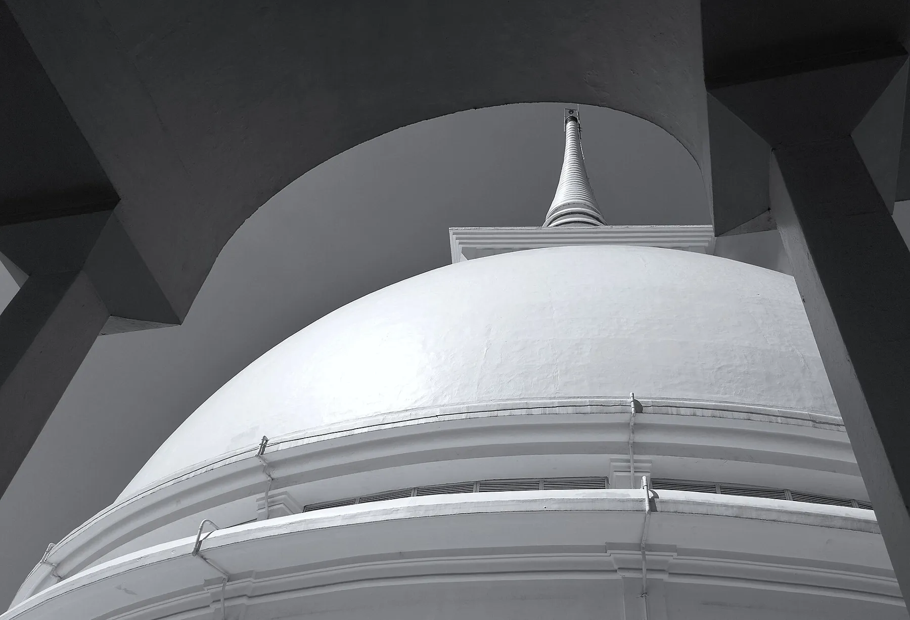 Looking up at the white dome and tall spire inside the hollow stupa at Kalutara Bodhiya, framed by dark concrete arches.