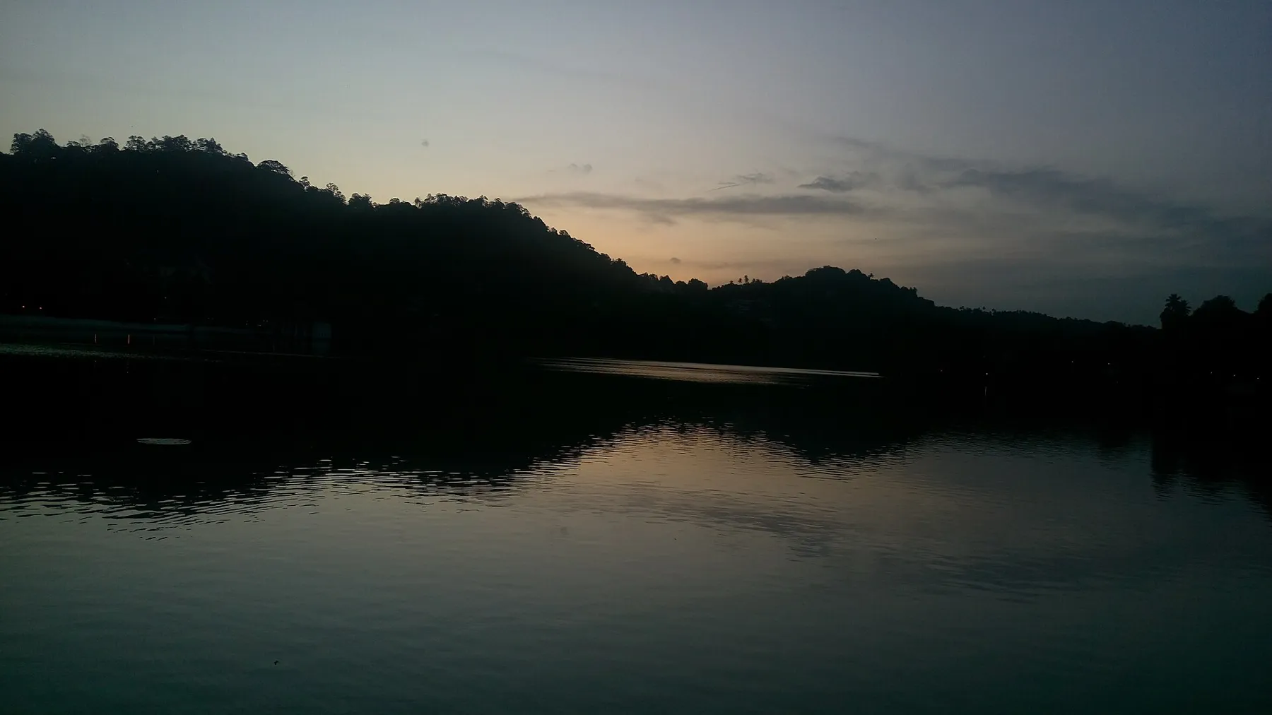 Kandy Lake in the soft low light of early morning, with the water still and dark trees along the shore.