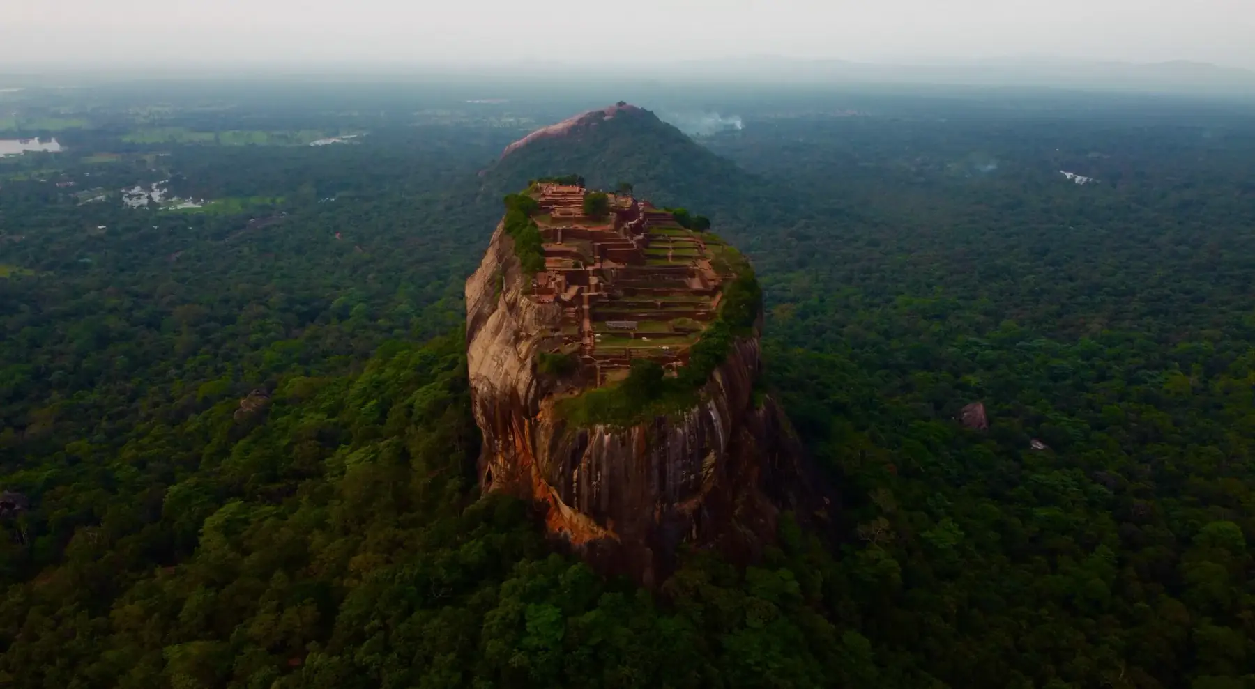 Aerial view of Sigiriya Rock rising sheer from flat green forest.